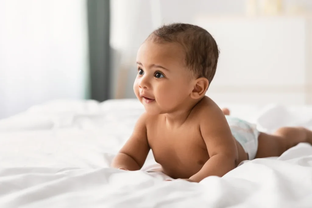 Bebé deitado de barriga para baixo, a sorrir, numa cama de lençóis brancos